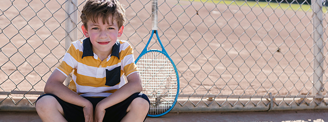 Niño sentado descansando en una cancha de tenis