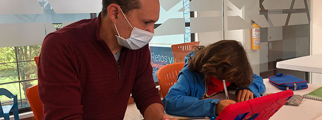 Adulto sentado en una mesa con un niño que sostiene una tablet