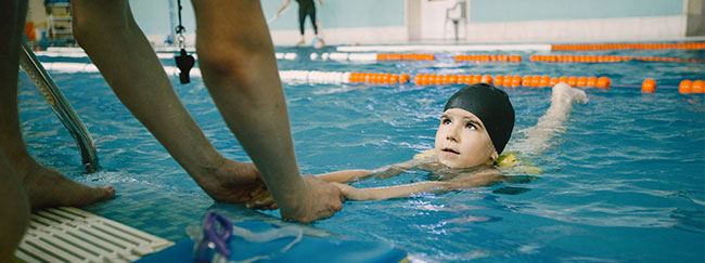 Niño aprendiendo a nadar con la ayuda de un adulto
