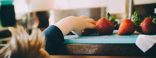 Niño estirando la mano para tomar una fresa de la mano