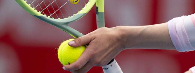 Raqueta de tenis junto con pelota sostenida por una mano